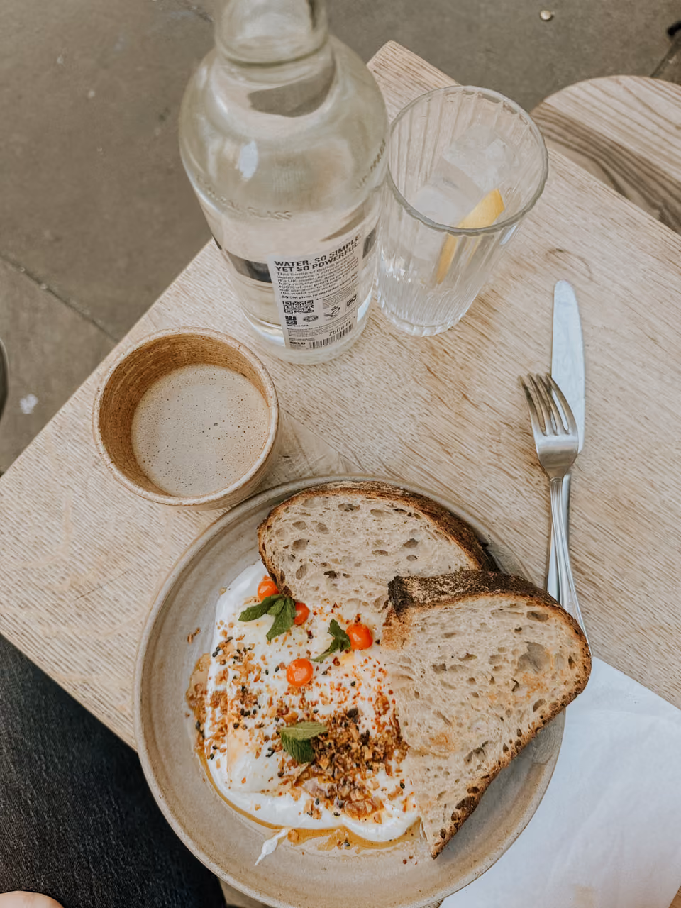 Plate with two slices of bread, whipped topping with herbs, alongside a cup of coffee and bottle with lemon water glass.