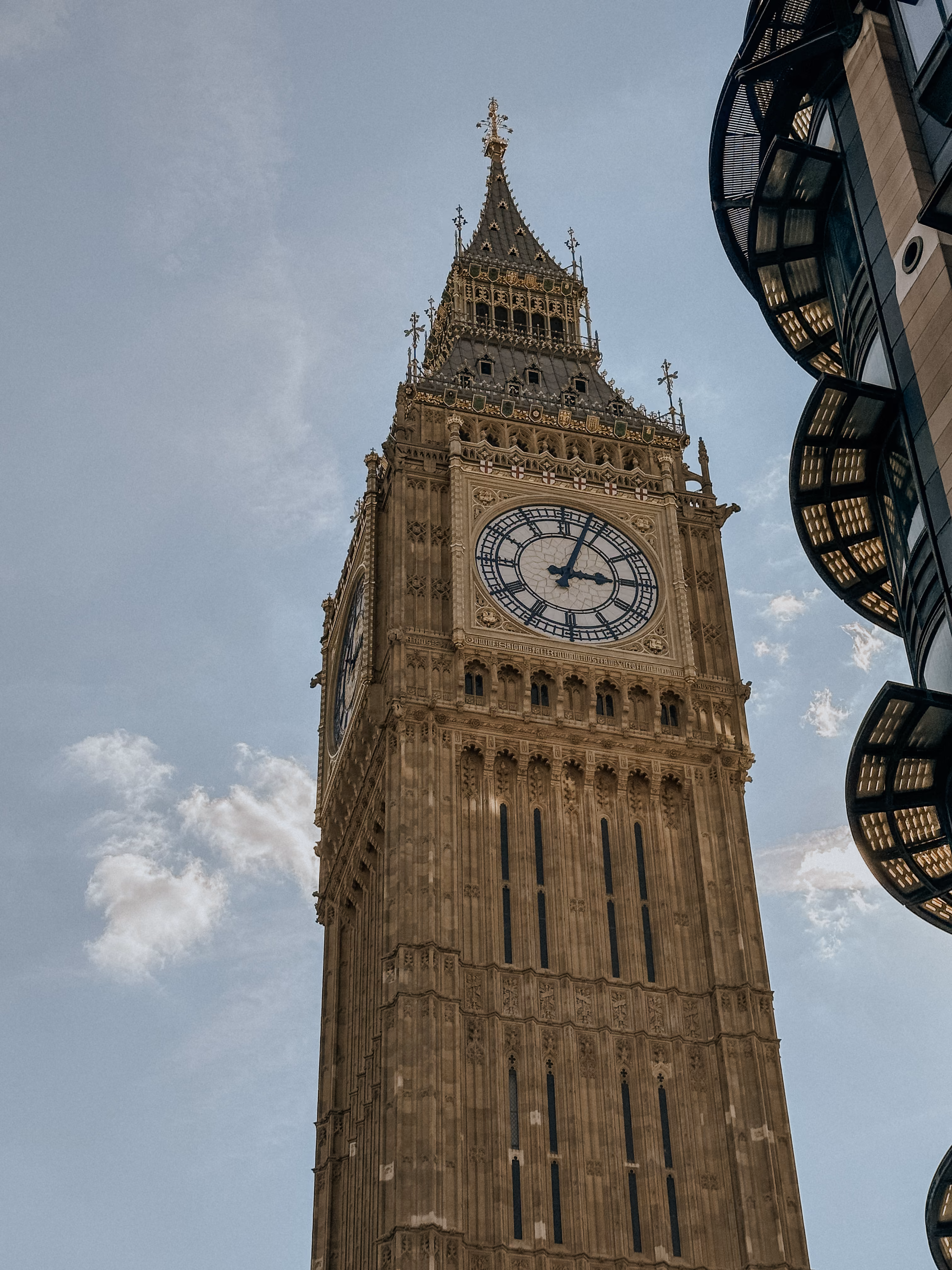 Big Ben clock tower in London against a clear blue sky with part of a modern building visible.