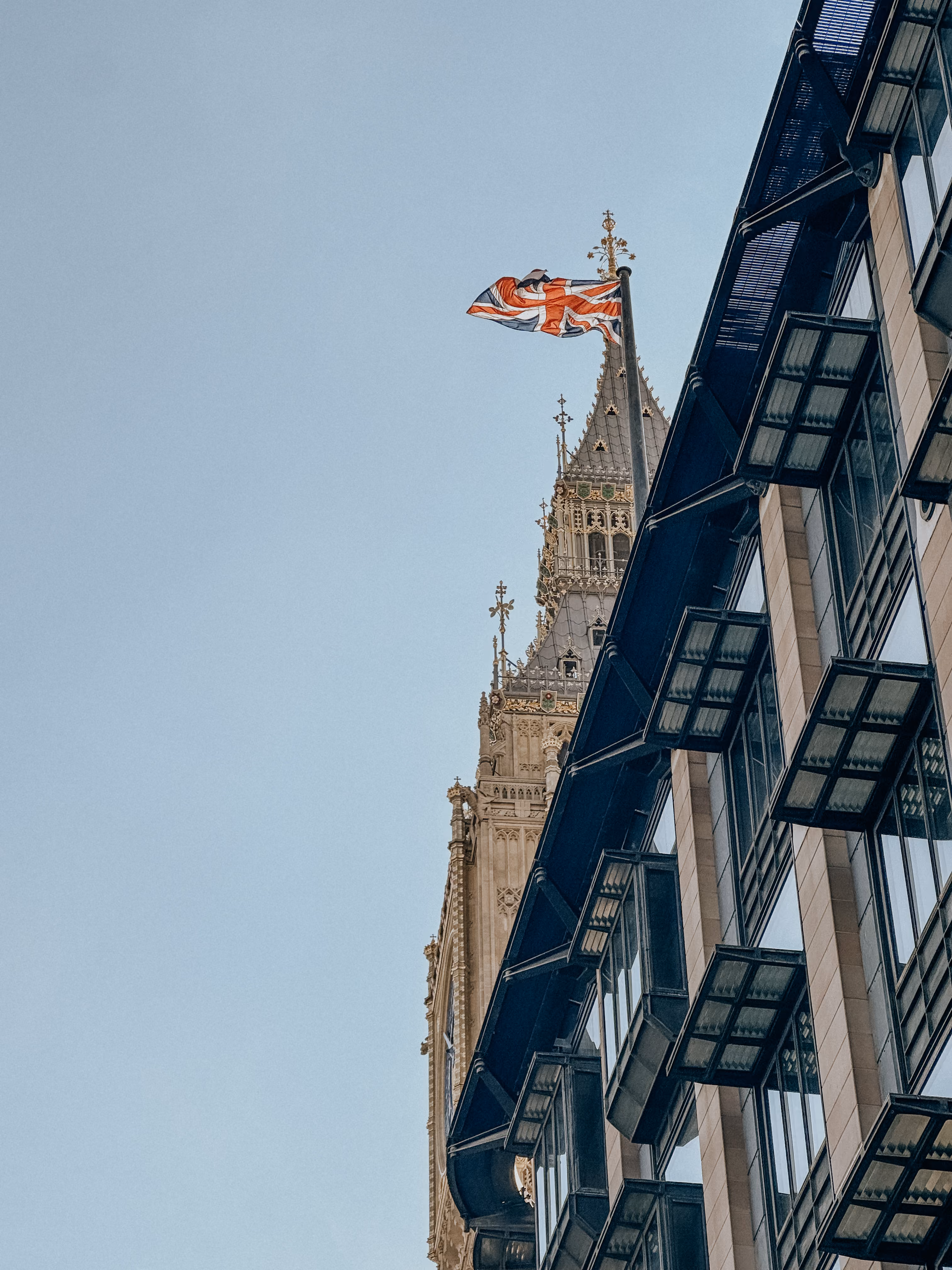Union Jack flag flies beside ornate clock tower with gothic architectural details in London.