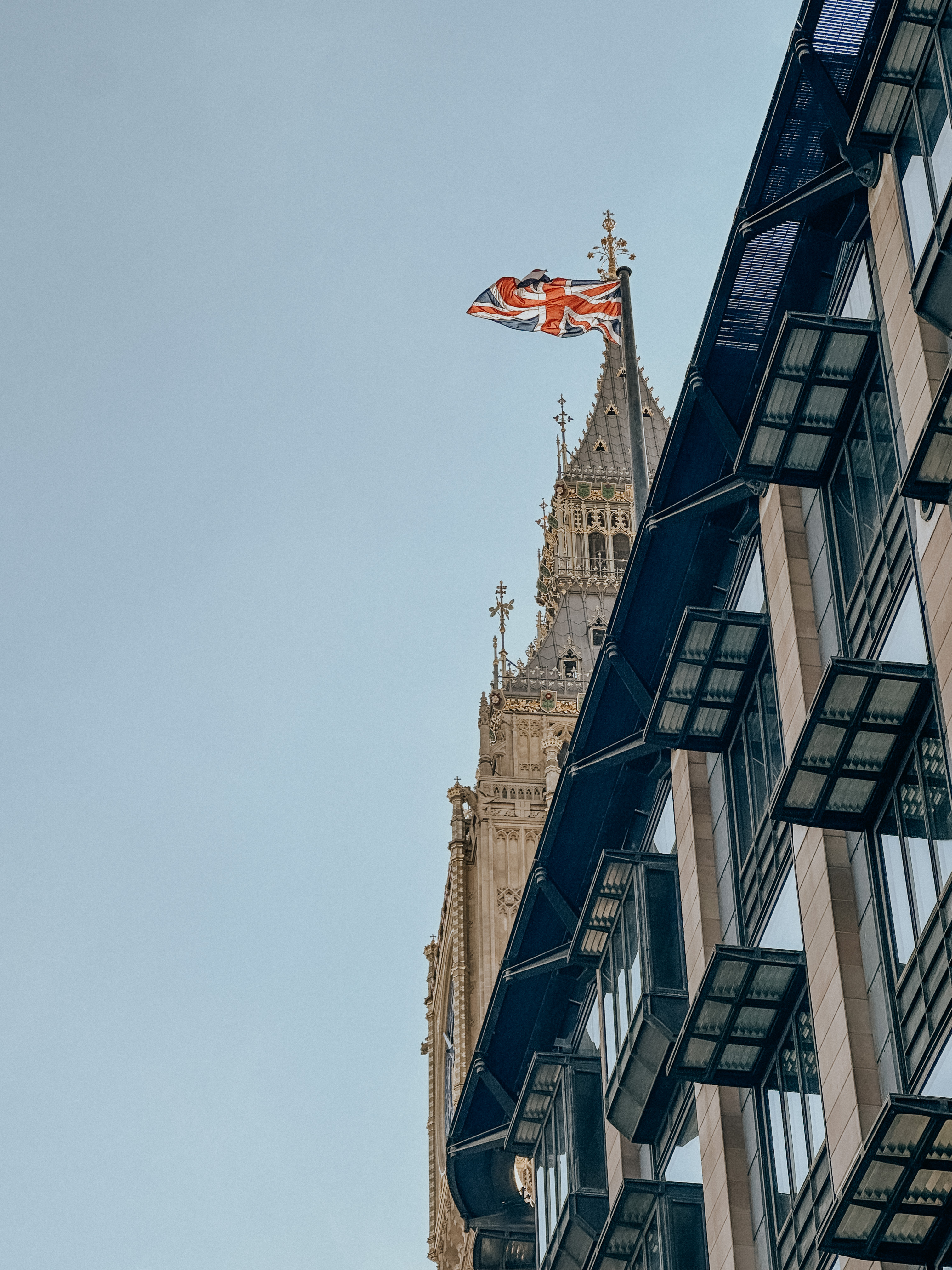 Union Jack flag flies beside ornate clock tower with gothic architectural details in London.