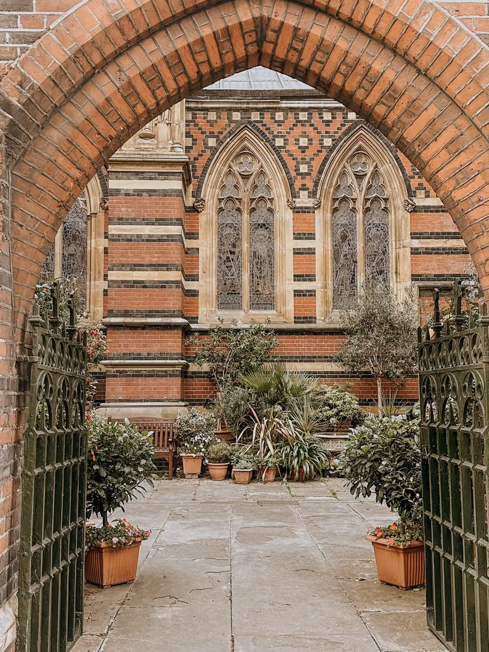 Arched brick entryway opening to a garden with plants and bench before stained glass windows.