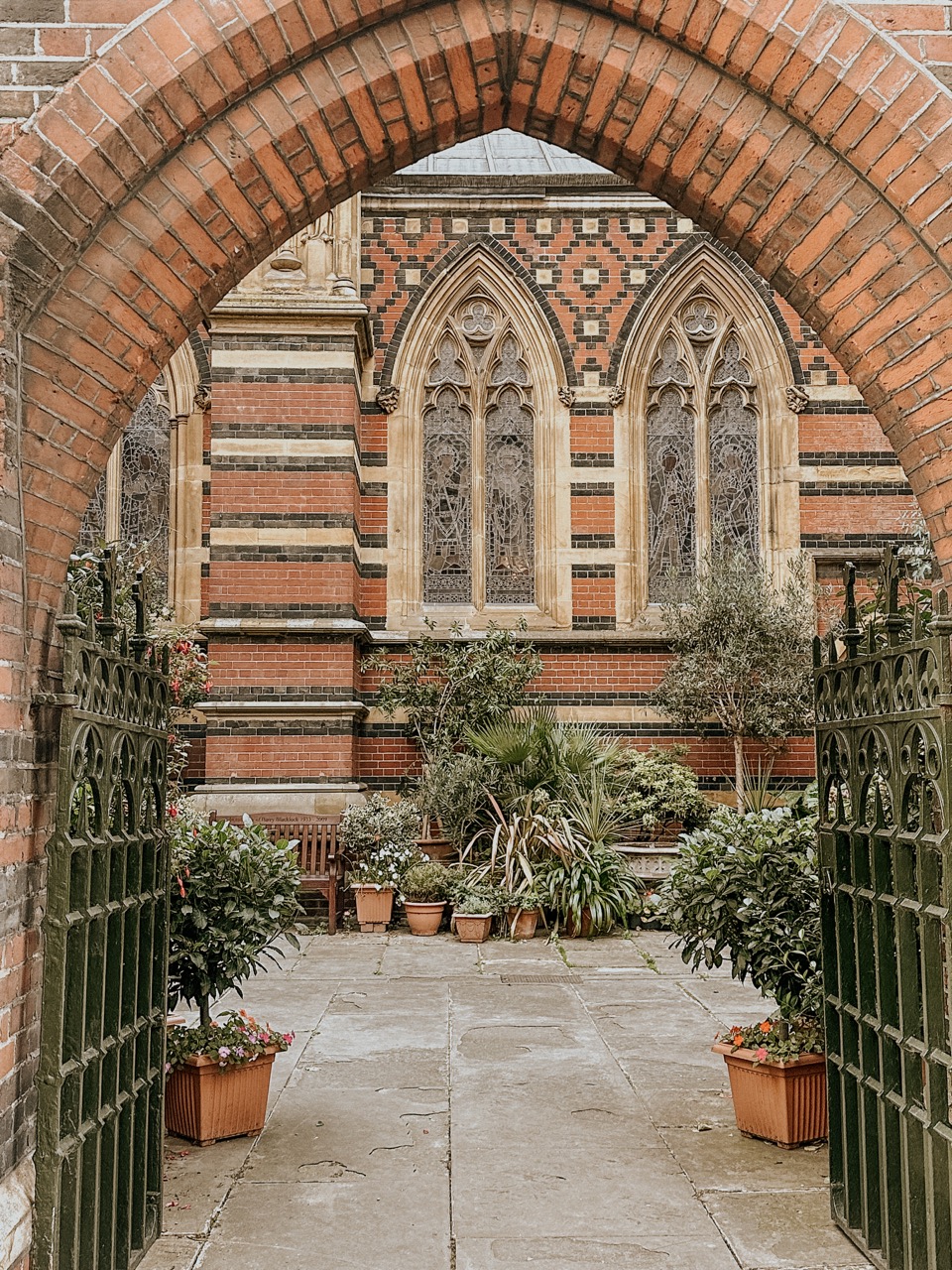 Arched brick entryway opening to a garden with plants and bench before stained glass windows.