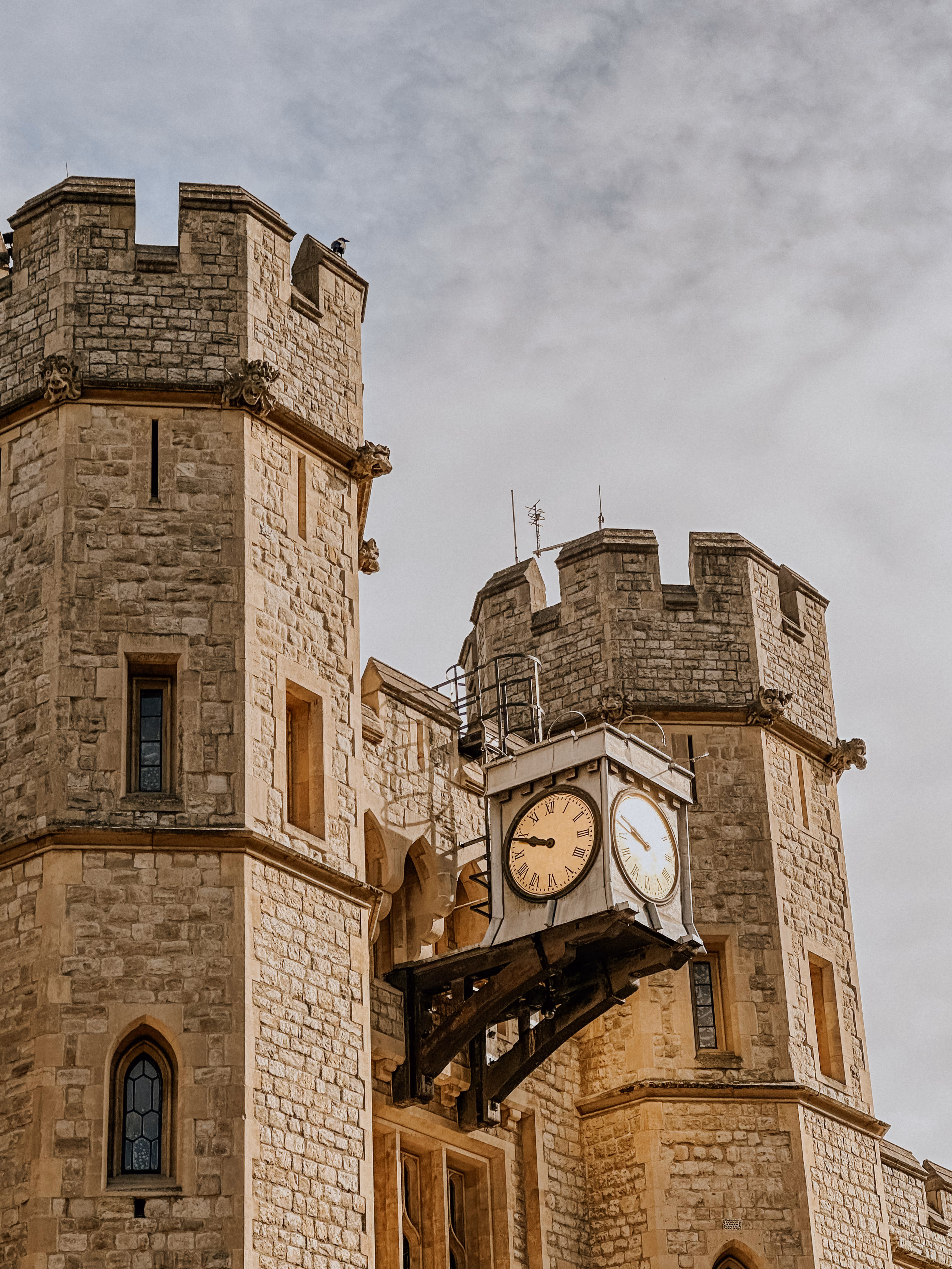 Stone castle towers with a large clock showing 7:17 mounted between them under a cloudy sky.