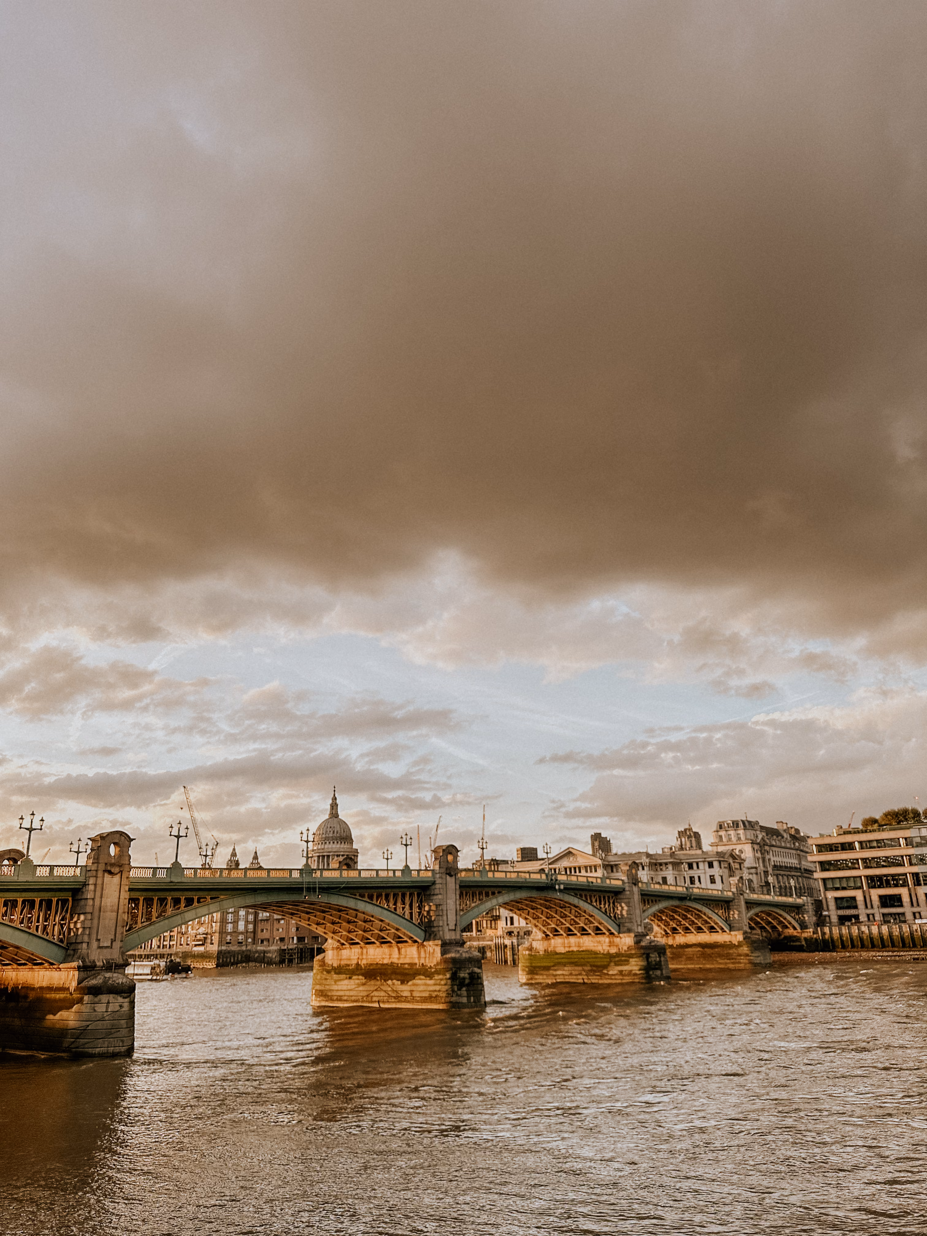 View of a historic arched bridge over a river with city buildings and a domed structure in background.