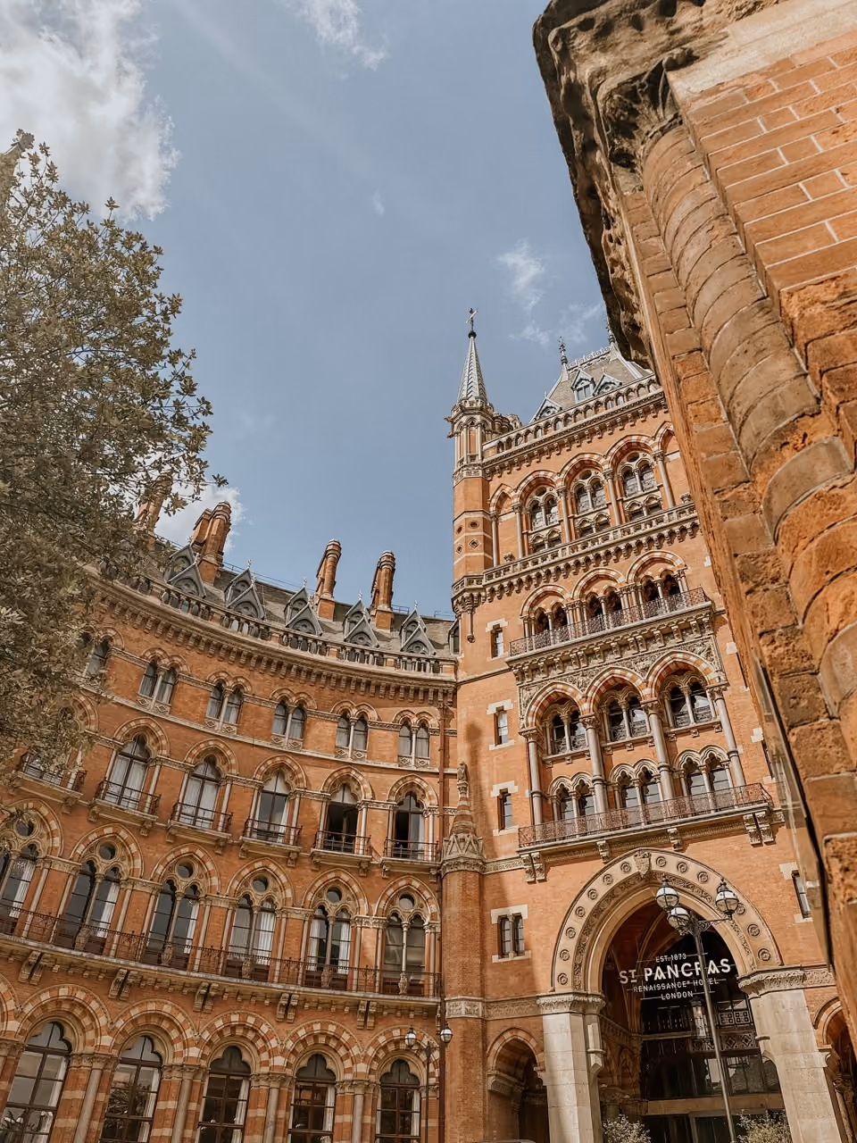 Historic red brick St. Pancras Renaissance Hotel building with gothic spires under a partly cloudy sky.