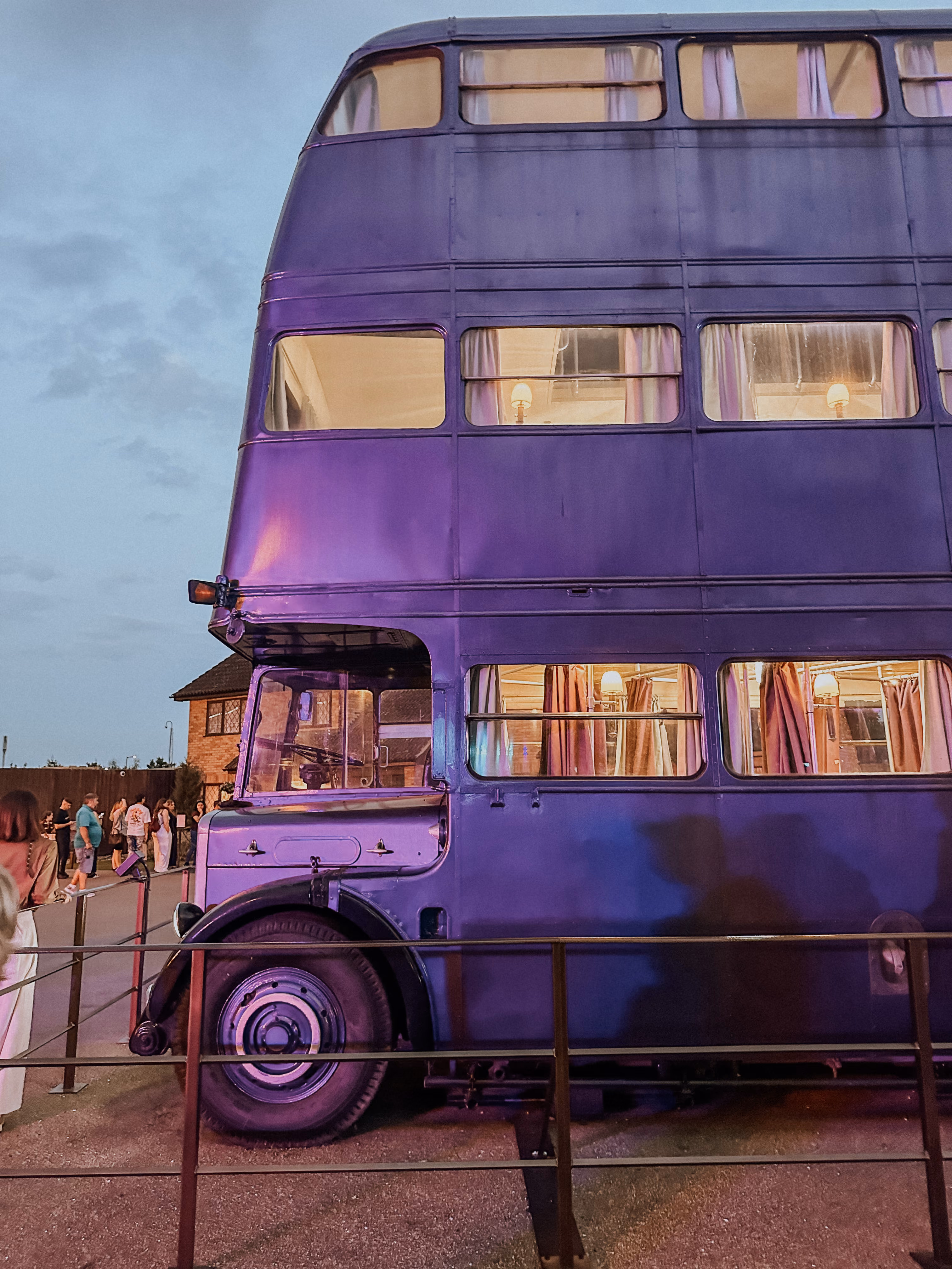 Purple vintage double-decker bus with lit lamps inside parked outdoors at dusk.