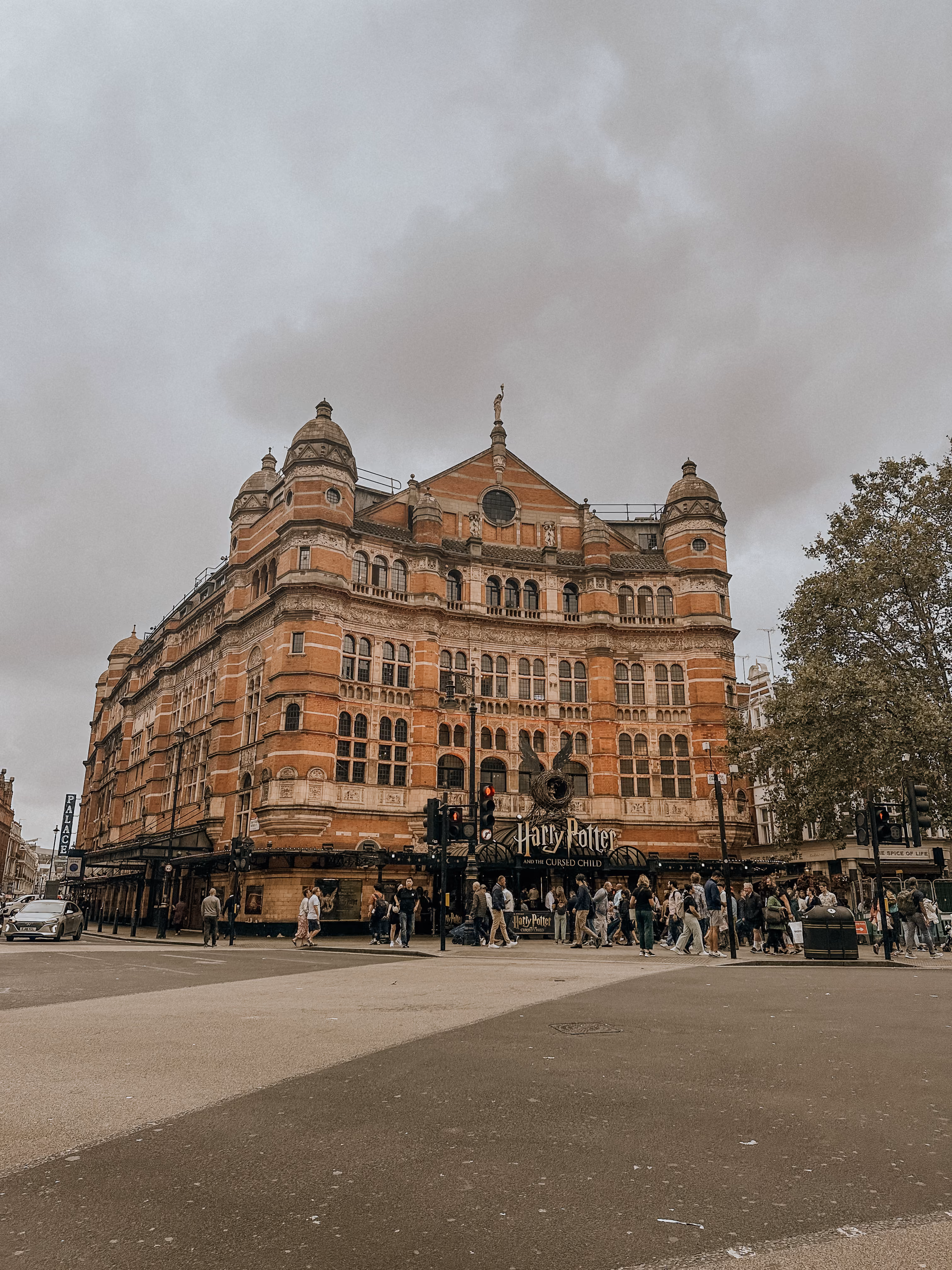 Historic brick building with 'Harry Potter and the Cursed Child' theater sign and crowd outside on a cloudy day.