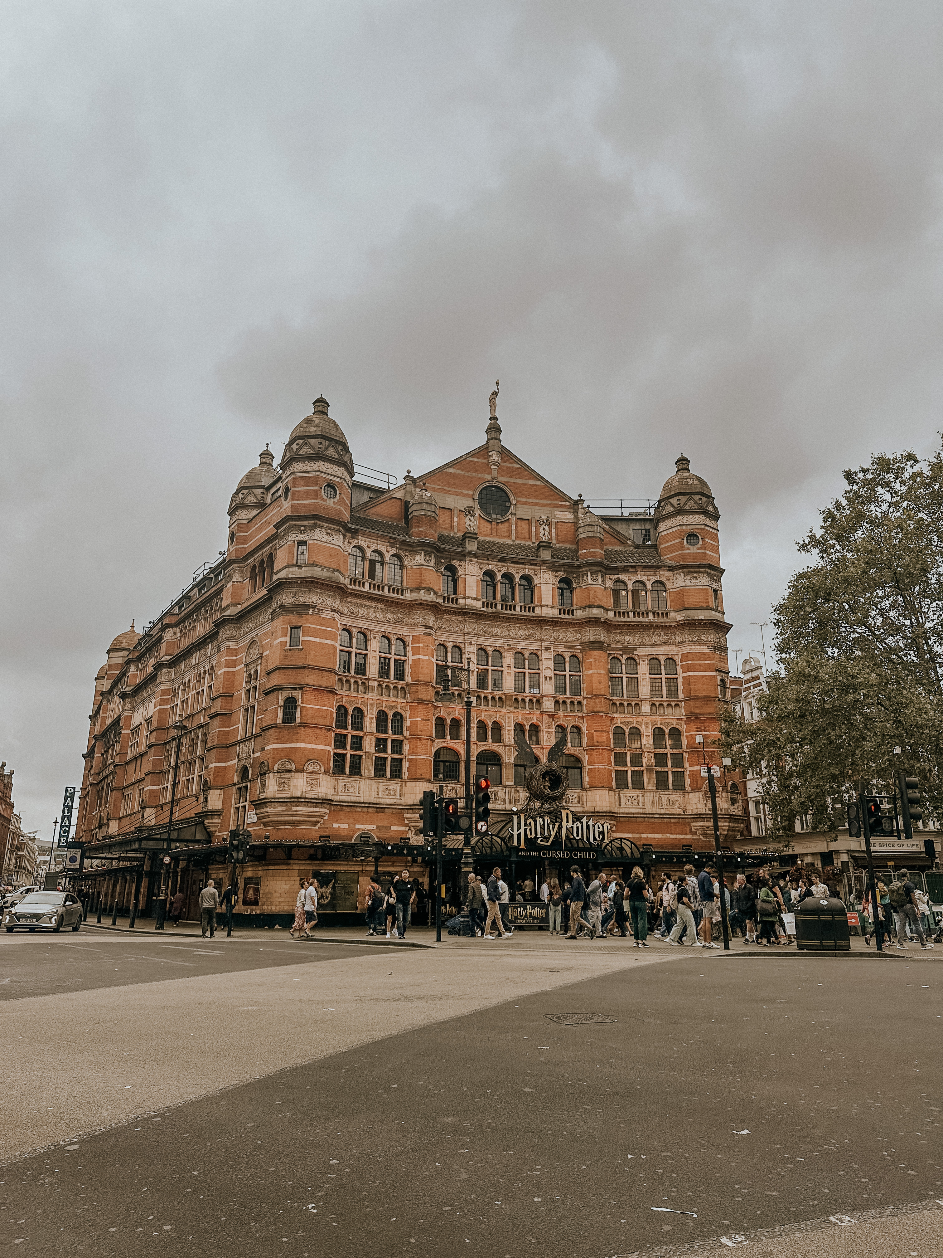 Historic brick building with 'Harry Potter and the Cursed Child' theater sign and crowd outside on a cloudy day.