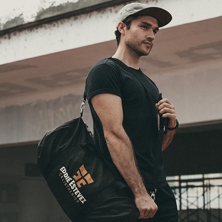 Eddie Estevez Calisthenics branded duffel bag mockup showing copper logo print on black travel gym bag carried by model outside urban training area