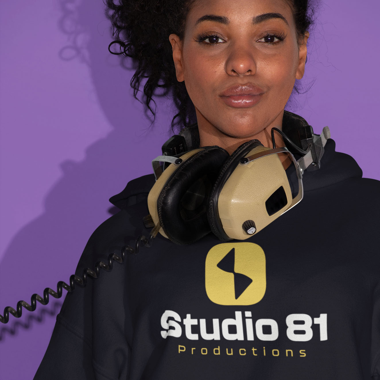 Pullover hoodie mockup displaying Studio 81 Productions yellow icon and white wordmark on black fabric worn by female model with studio headphones