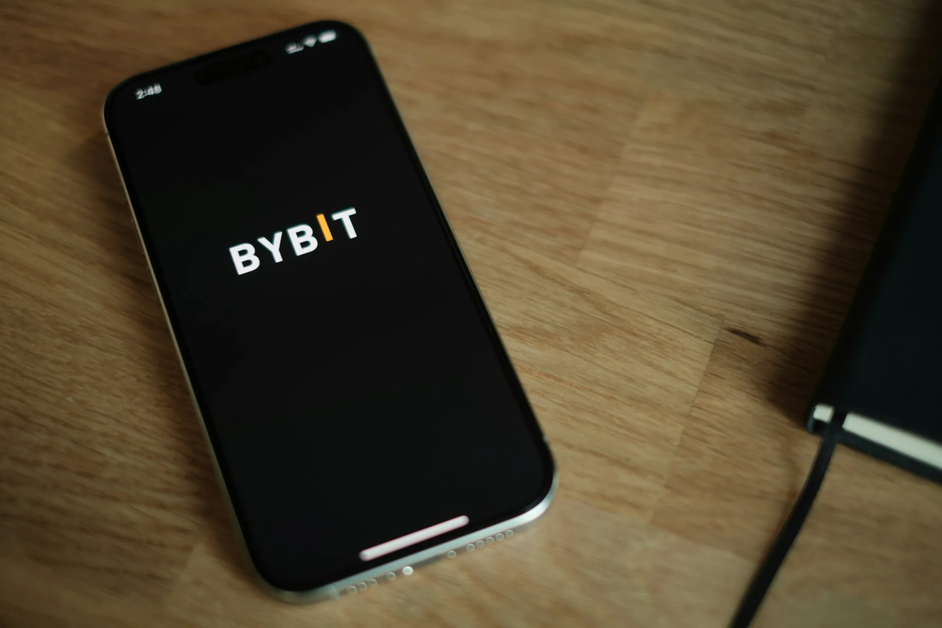 Smartphone on a wooden desk displaying the Bybit exchange logo