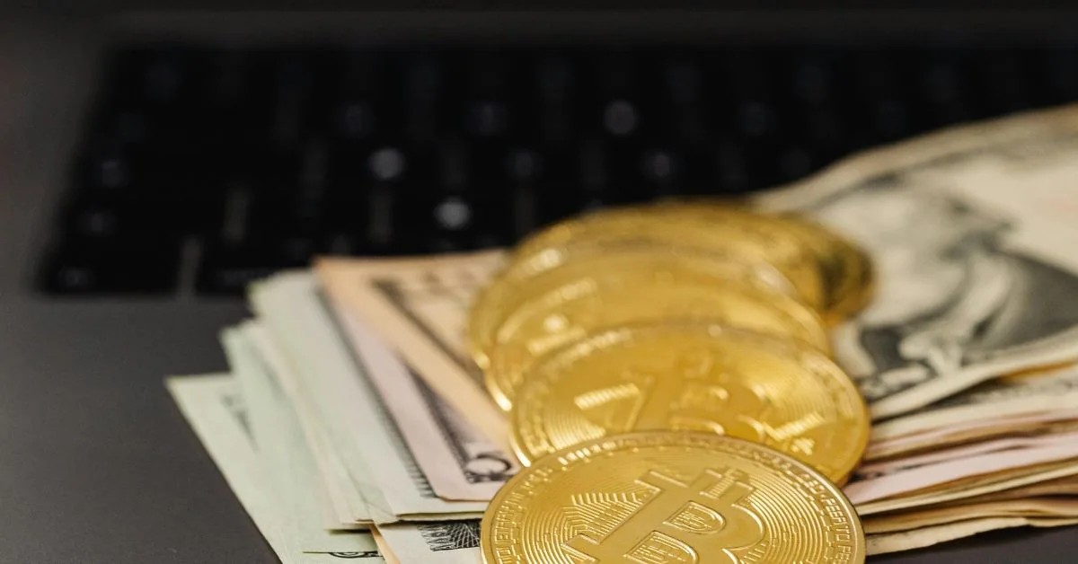 Gold Bitcoin coins and US dollar notes lying on a laptop keyboard
