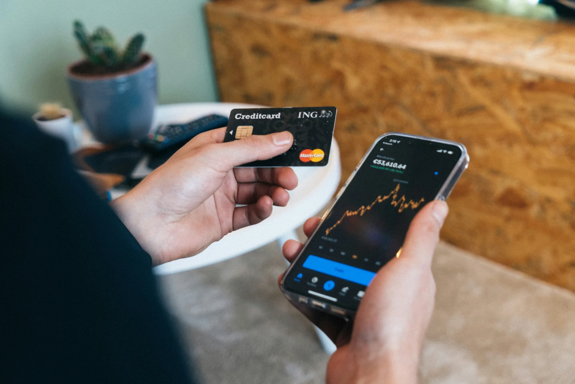 Hands holding a credit card and a phone showing a crypto price chart
