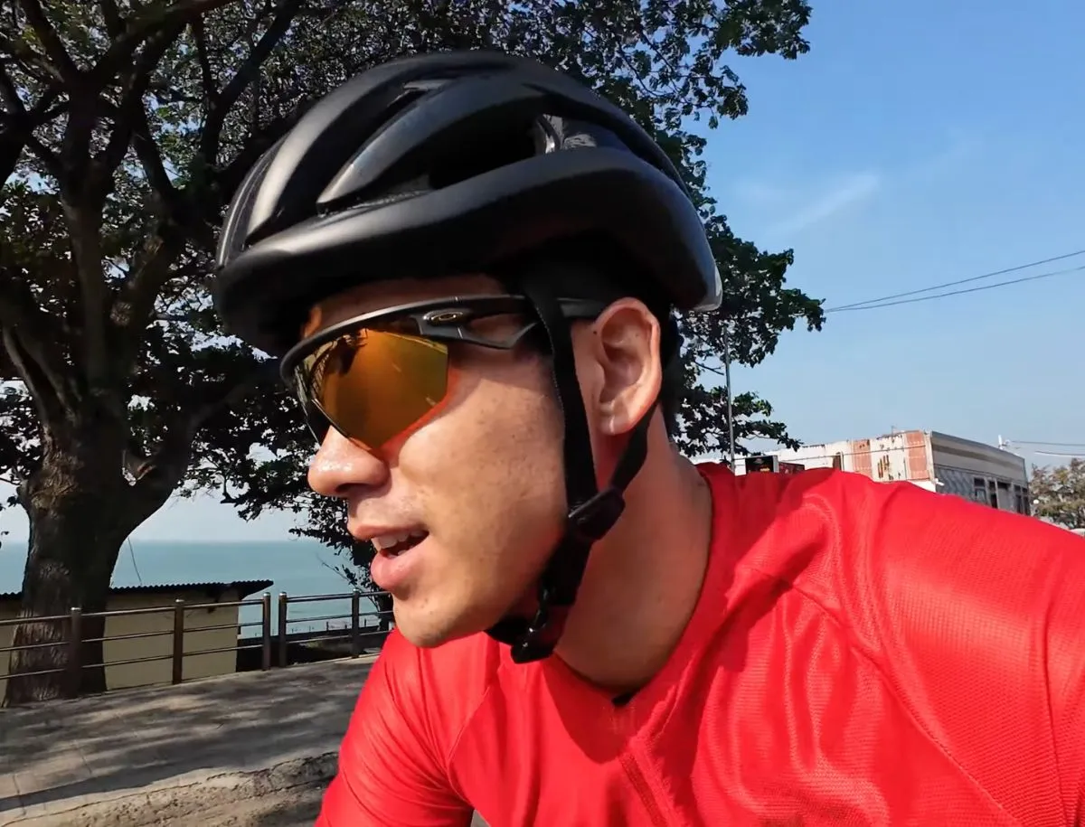 Close-up of a male cyclist wearing a black road cycling helmet and Oakley sunglasses with orange lenses while riding along a coastal road