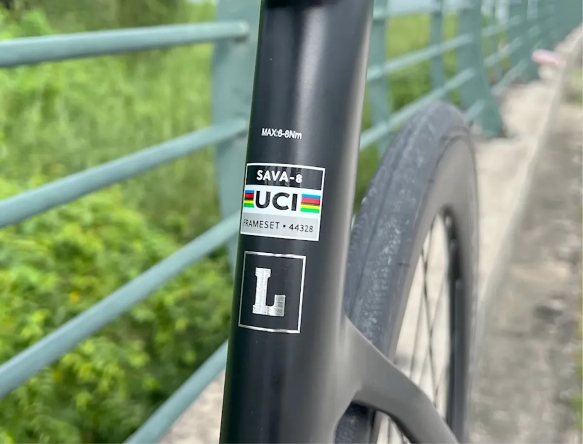 SAVA A7L Pro carbon frame showing UCI-approved SAVA-8 frameset sticker and size L label on the seat tube, with front wheel visible in background
