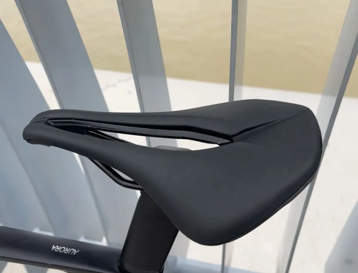 Close-up of SAVA DE99 black road bike saddle showing central relief channel, flat profile, and minimal padding, mounted on the SAVA A7L Pro with Aurora seatpost visible below