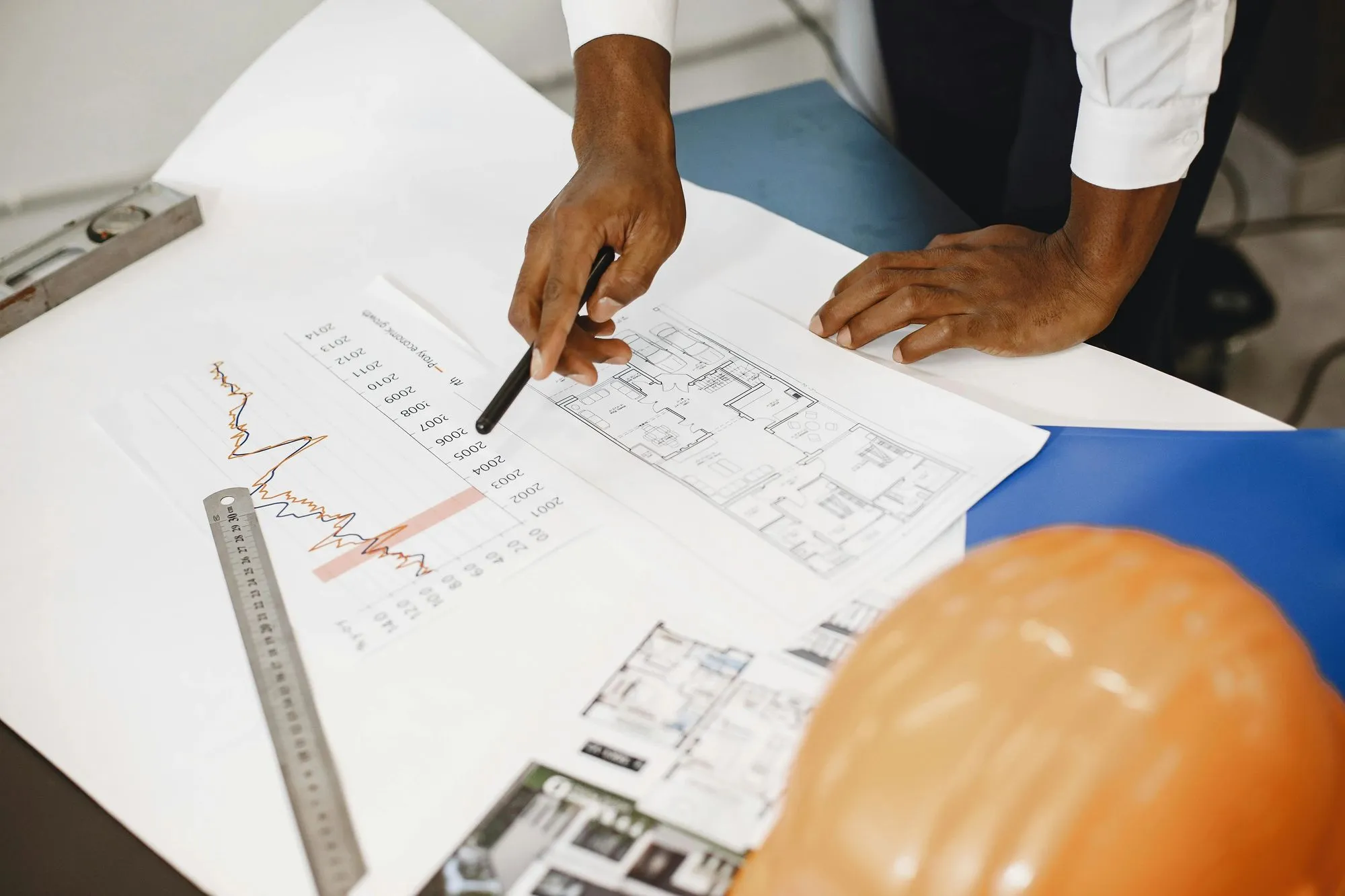 Construction plans and hard hat on a table, representing bookkeeping and document control for construction and manufacturing businesses