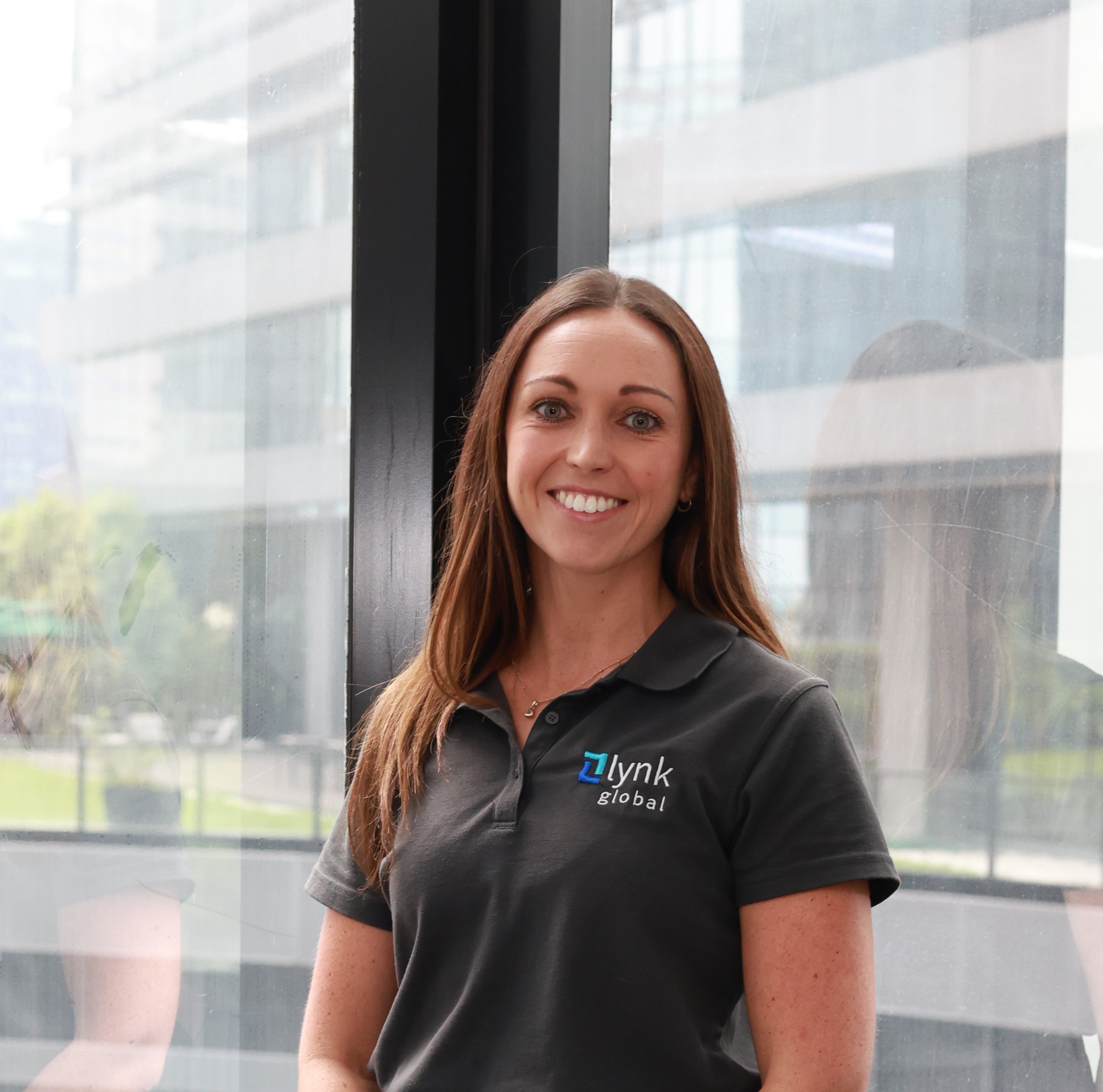 Jessica, Co-Founder and Director of Lynk Global, smiling in front of a modern office window.