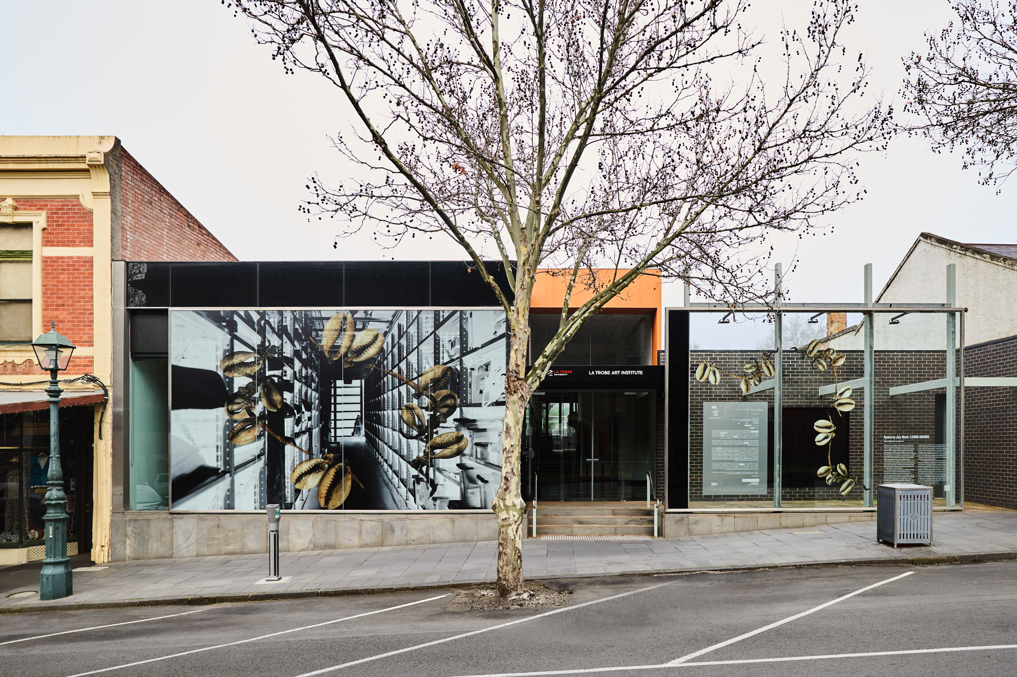 Wide view of the full gallery frontage: the large window artwork, black entrance, and adjacent glass screen with shell graphics and text.
