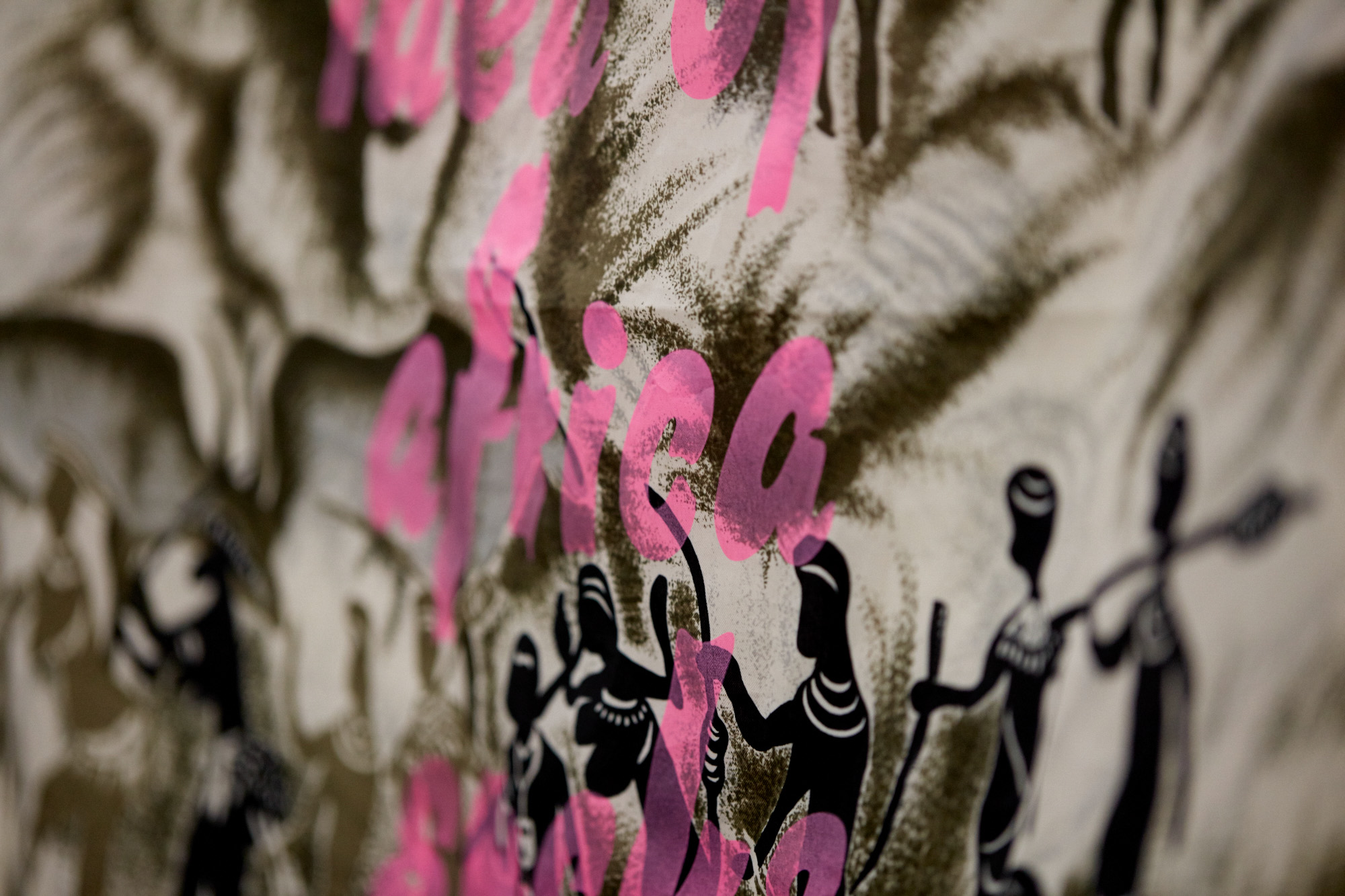 Close-up detail of the scarf showing pink hand-lettered text layered over dark silhouetted figures and smoky brushwork on cream fabric.