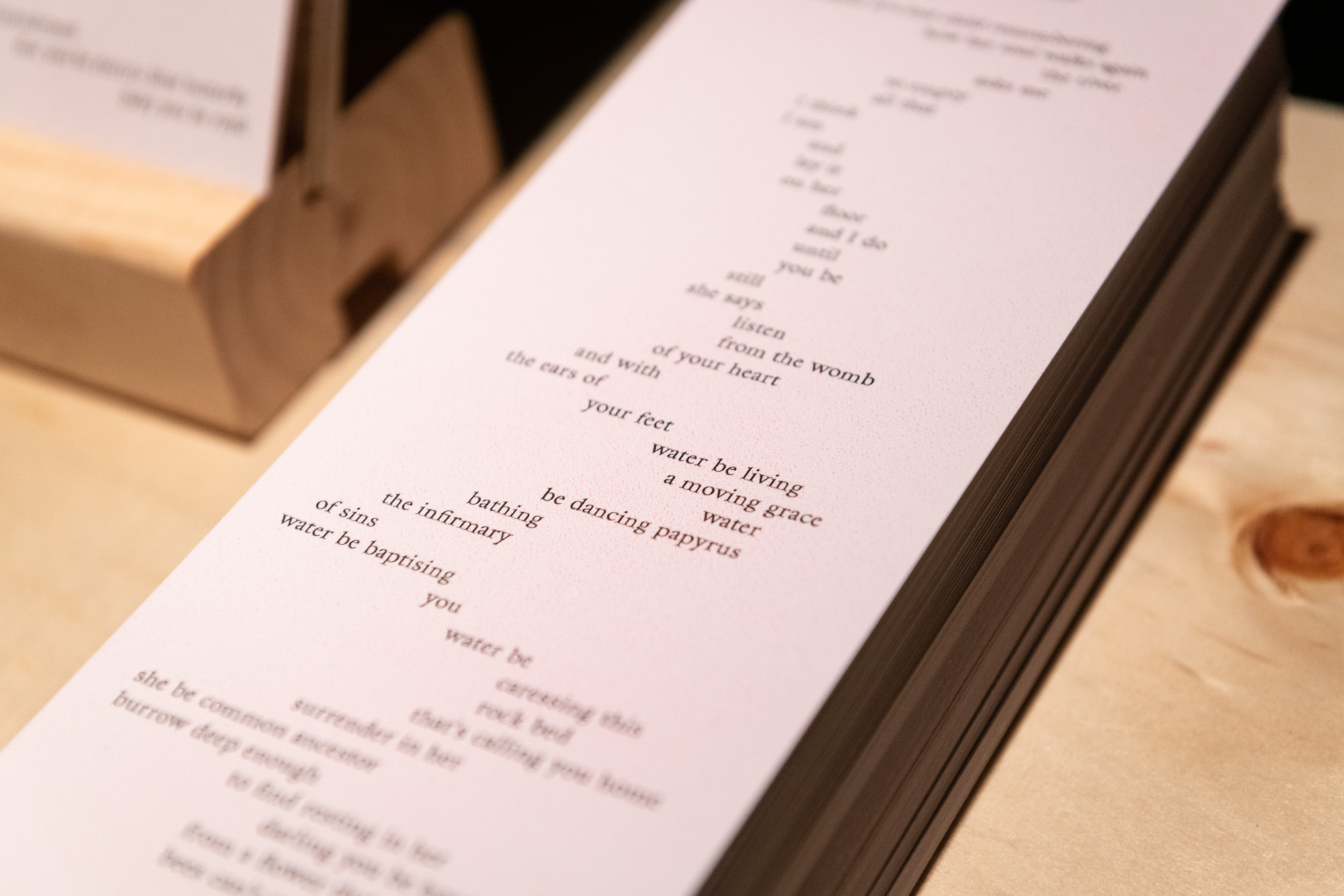 Close-up of the poem sheet, its lines drifting in steps down the pale pink page, including the words "water be living / a moving grace / water / be dancing papyrus."