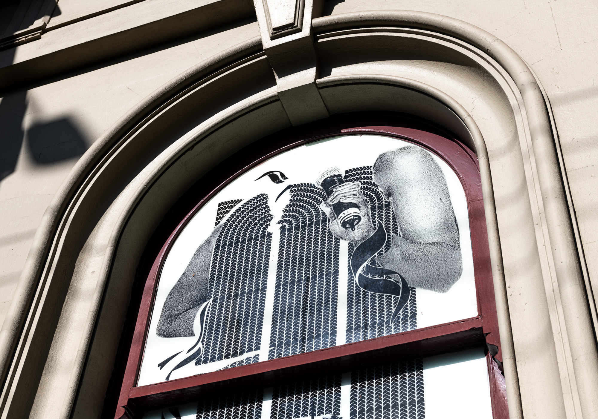 Detail of an arched window artwork: a black-and-white collage of two arms of a Black woman raised above a body of dense braid-weave pattern, one hand gripping a microphone, with a ribbon curling between them.