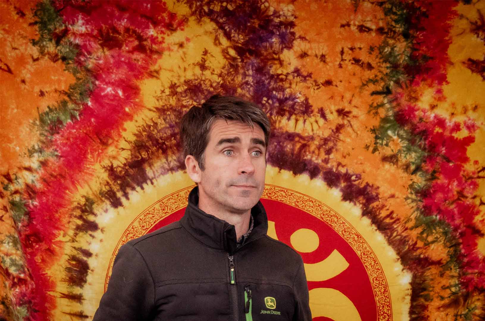 A festival goer poses for a photo with a beautiful coloured tie-dye backdrop in reds and orange colours