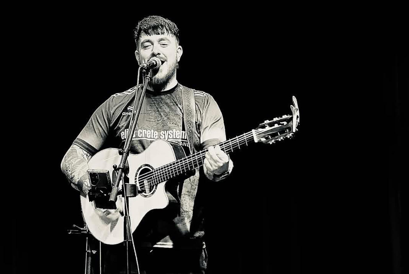 Singer Gearoid McCarthy stands alone on stage playing guitar and singing.