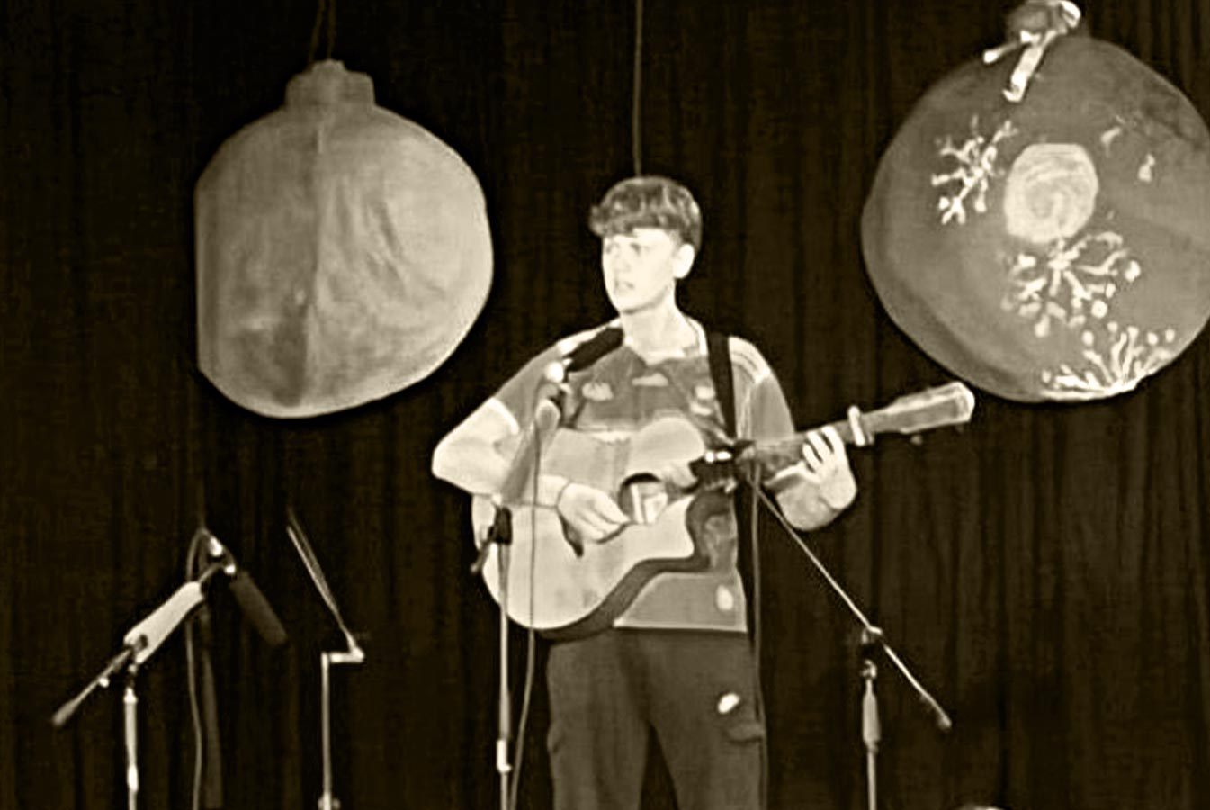 Rían Lynch standing, plays guitar and sings on stage