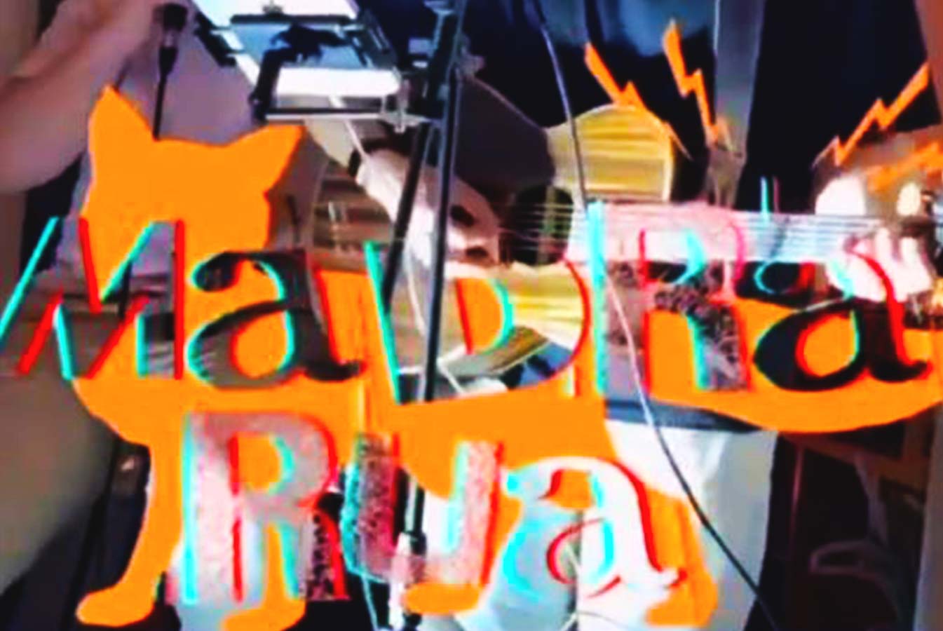 A graphic says Madra Rua in the foreground. A person plays guitar on stage in the background.