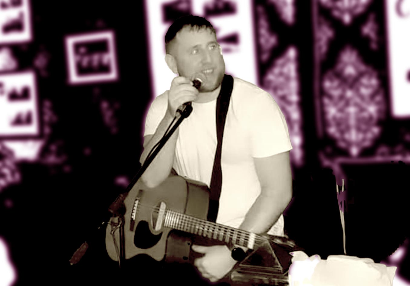 Eoin O'Kelly holds the mic, and guitar on stage.