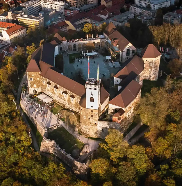 Aerial view of a historic stone castle with multiple towers and a central courtyard, surrounded by trees and urban buildings.