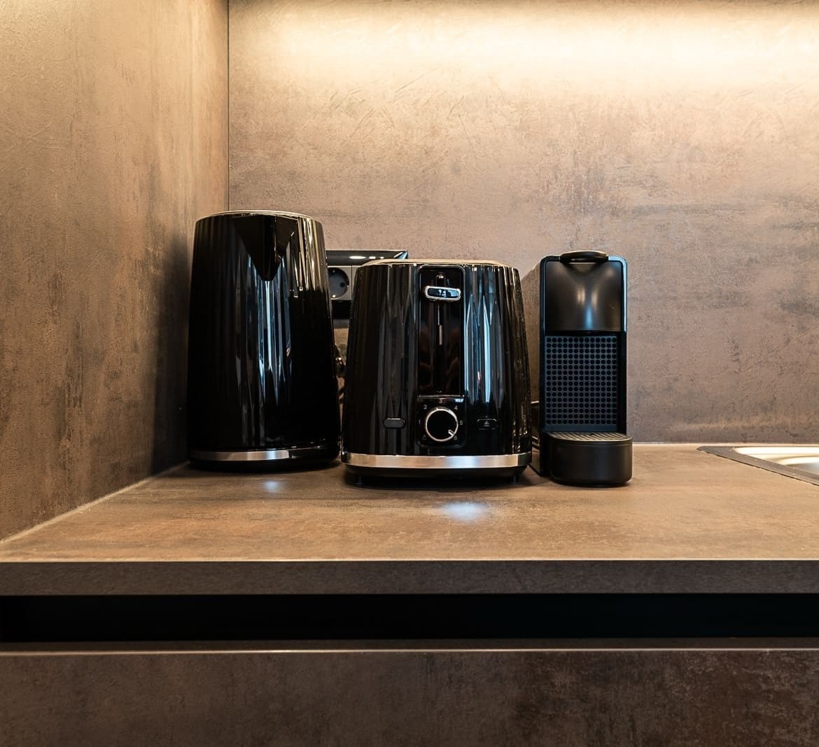 Black electric kettle, toaster, and coffee machine on a brown kitchen countertop against a beige textured wall.