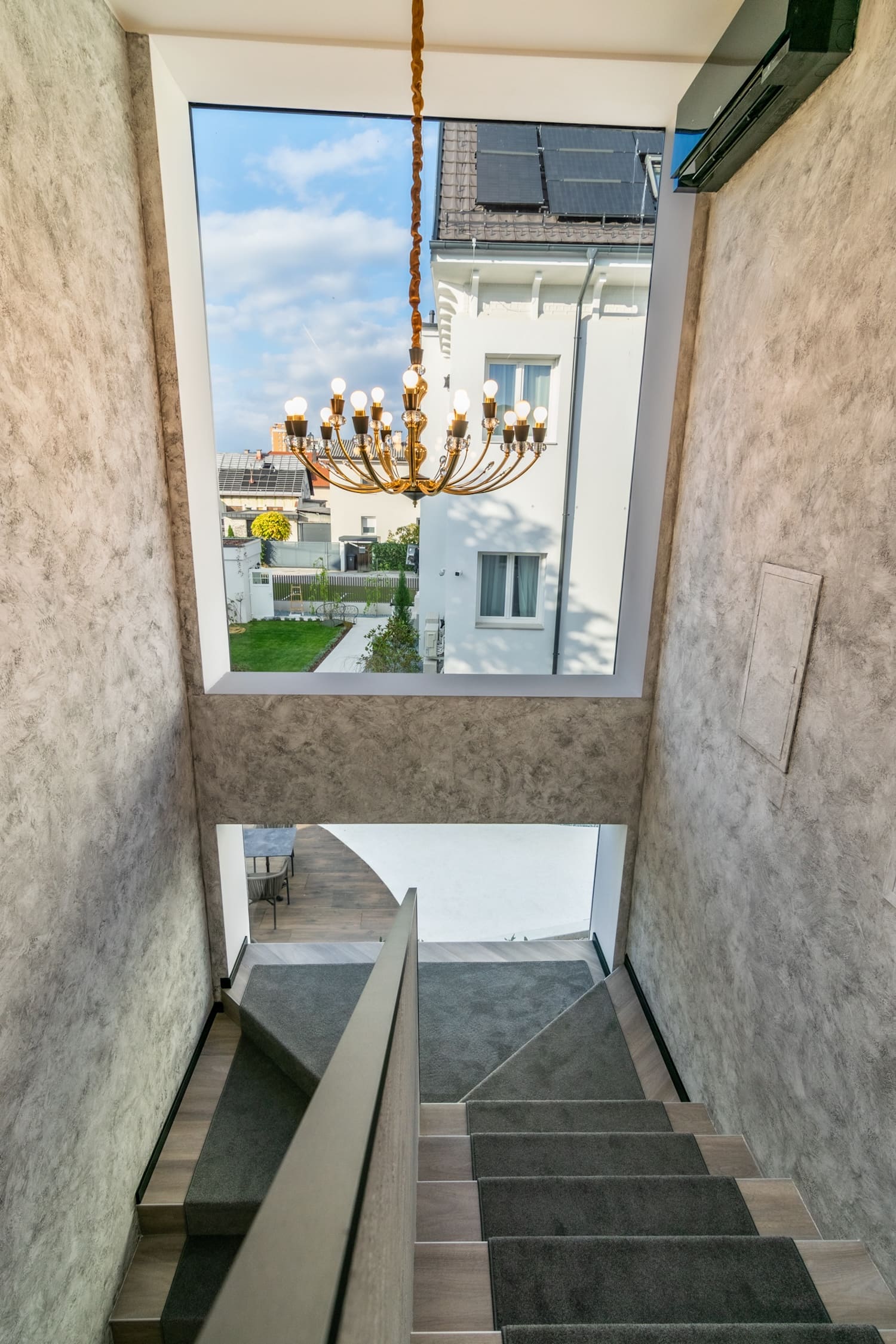 Carpeted staircase with a large window showing a residential building and hanging chandelier.