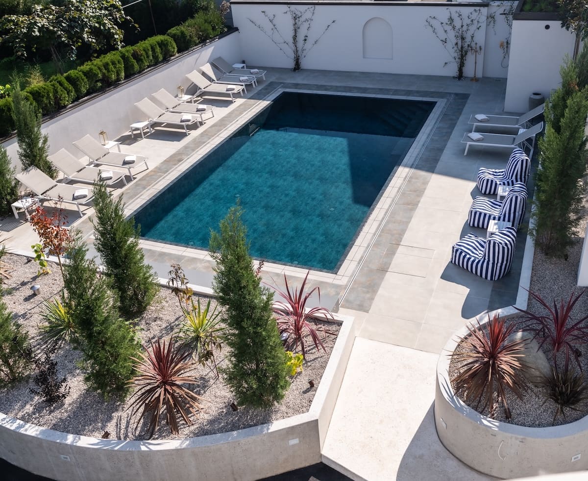 Rectangular outdoor swimming pool surrounded by lounge chairs and striped bean bag chairs with landscaped plants nearby.