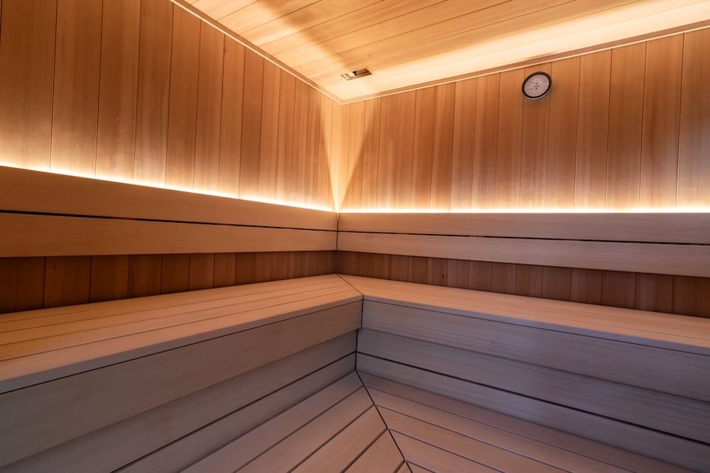 Empty wooden sauna interior with tiered bench seating and soft LED lighting along the walls.