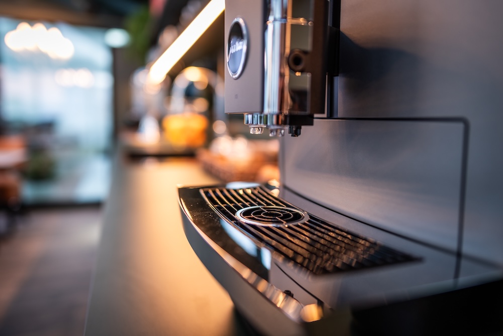 Close-up of a modern coffee machine with a drip tray in a softly lit kitchen or café setting.