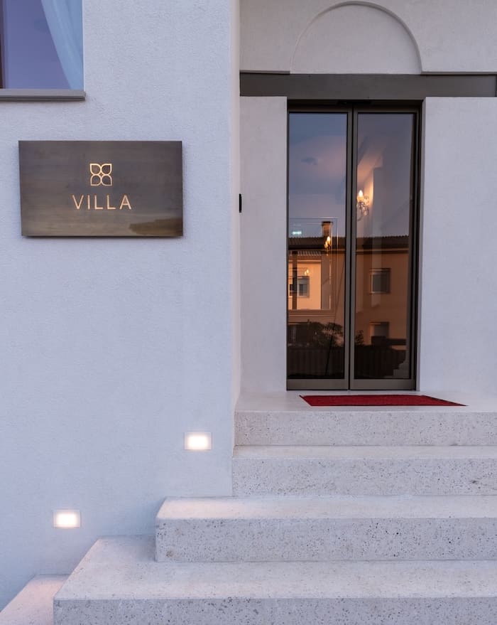 Exterior entrance of a villa with stone steps leading to glass double doors and an illuminated sign reading 'VILLA'.