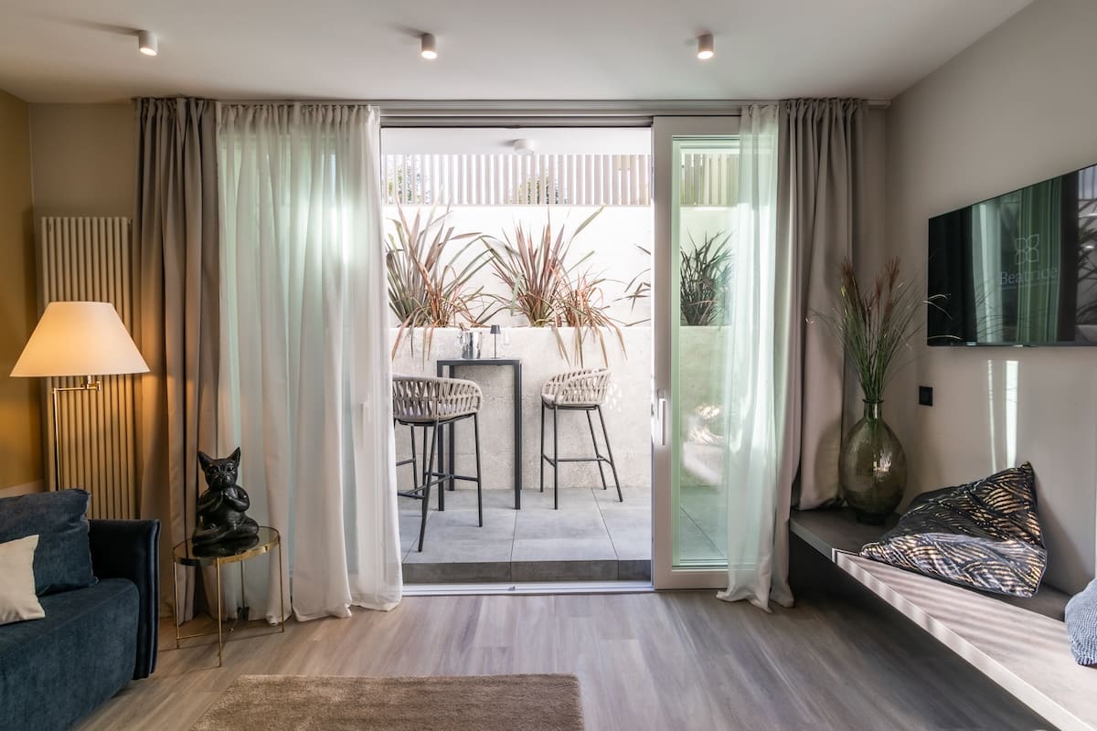 Modern living room with sliding glass door opening to a small patio with two bar stools and plants.