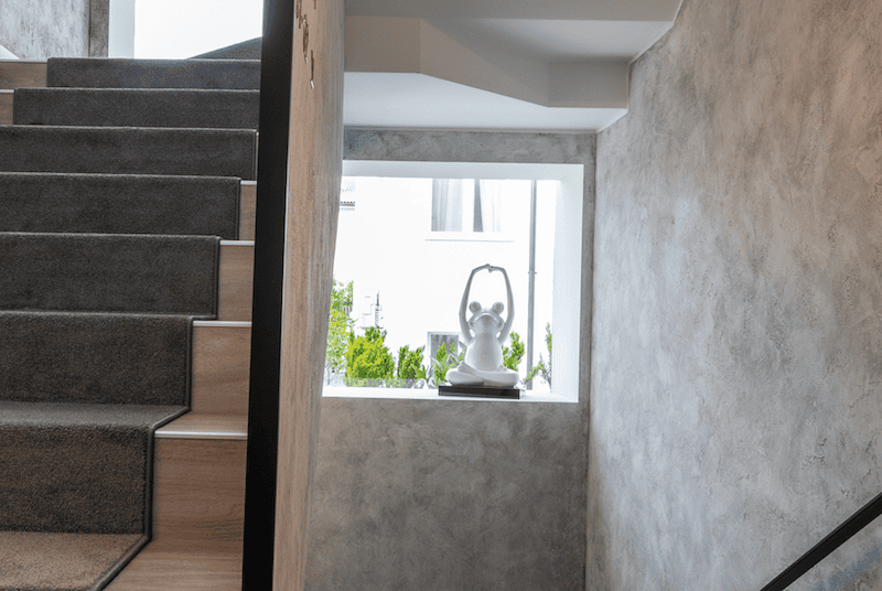 Indoor stairwell with gray carpeted steps and a window sill featuring a white decorative statue of a person in a yoga pose.