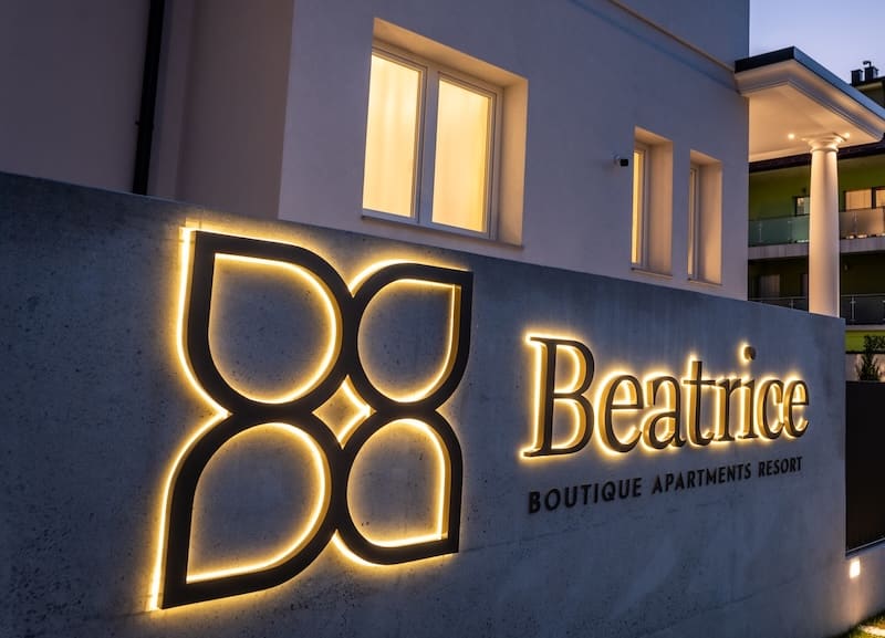 Illuminated sign for Beatrice Boutique Apartments Resort on a concrete wall outside a modern building at dusk.