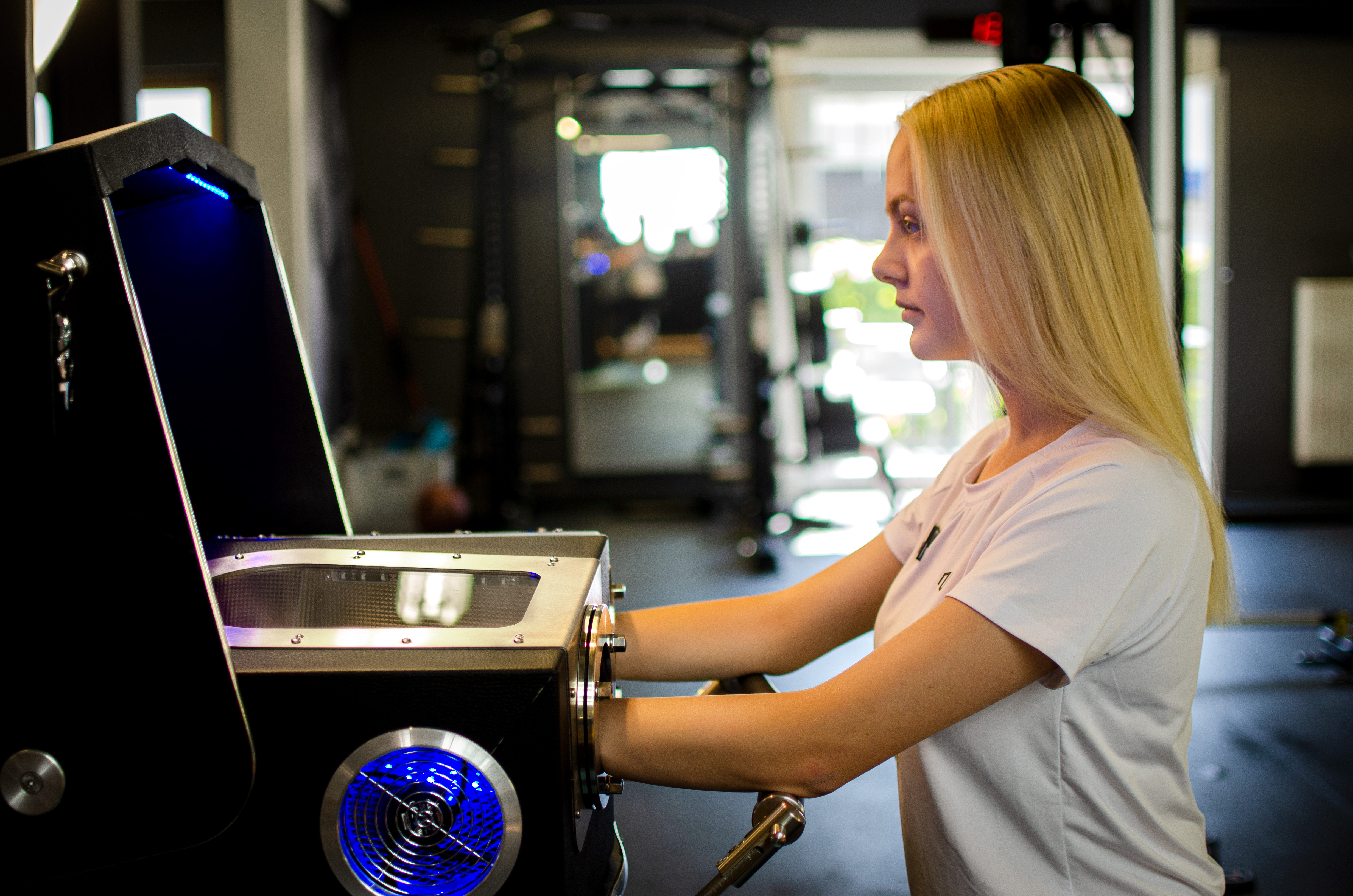 Frau nutzt in Fitnessstudio ein Gerät zur Hand- oder Armtherapie mit blauer Beleuchtung.