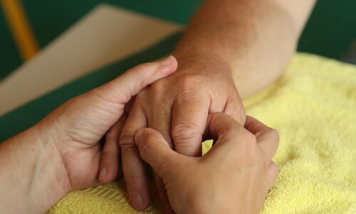 Eine Hand hält eine andere Hand und massiert sie sanft auf einem gelben Handtuch.