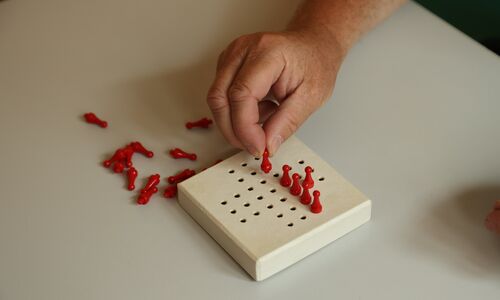 Hand platziert rote Spielfigur auf einem weißen Holzbrett mit kleinen Löchern in einer Reihe.