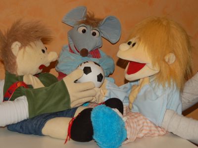 Drei Handpuppen sitzen zusammen, eine hält einen kleinen Fußball.