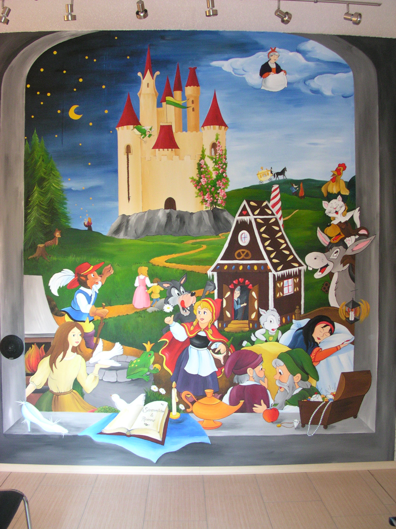 Bunte Wandmalerei mit einer Schlosskulisse und Figuren aus verschiedenen Märchen wie Rotkäppchen, Schneewittchen, Hänsel und Gretel, einem Wolf, einem Frosch, einem Zauberer, einem magischen Haus und anderen Märchencharakteren.