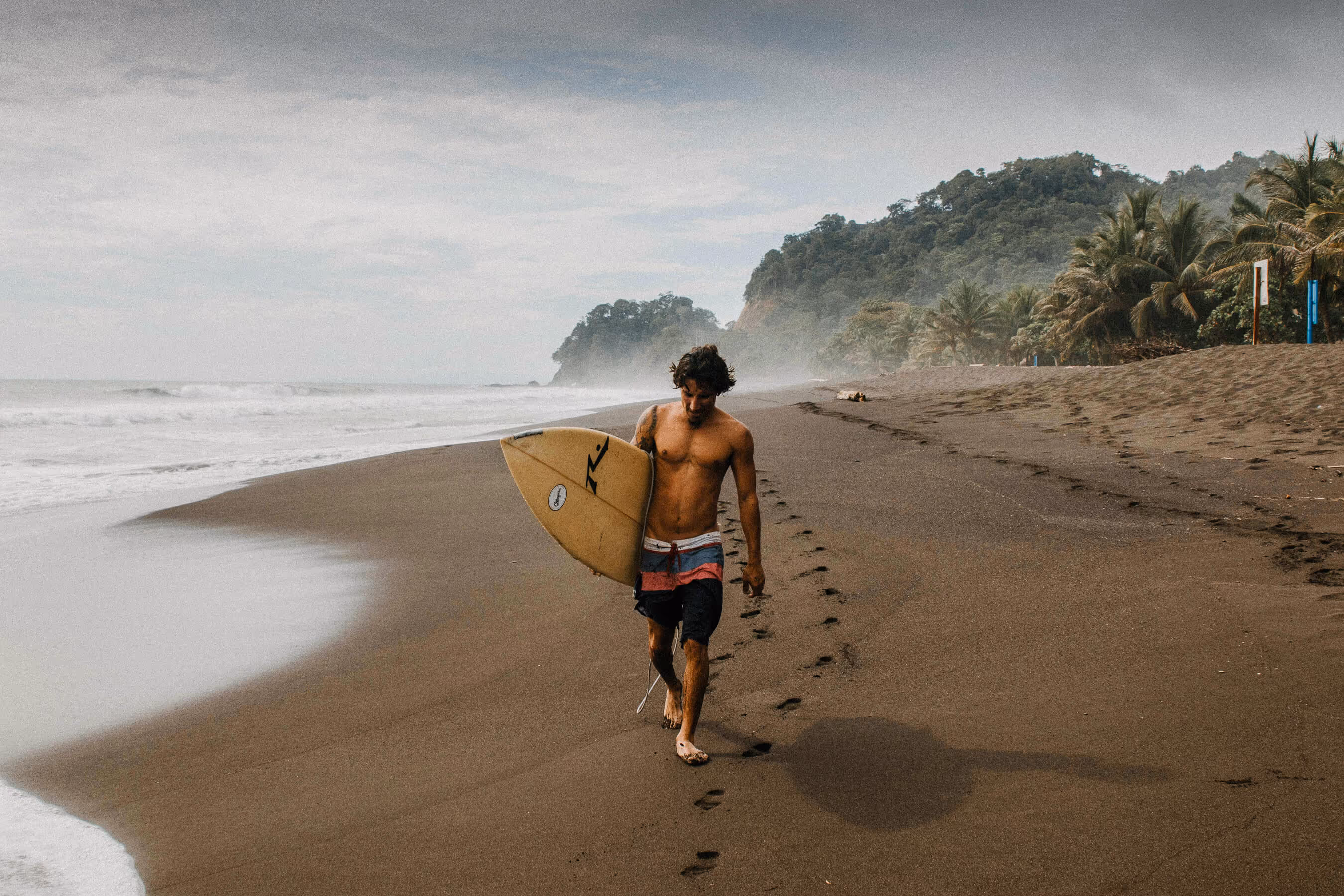 A surfer walking down the beach in Costa Rica with his surf board