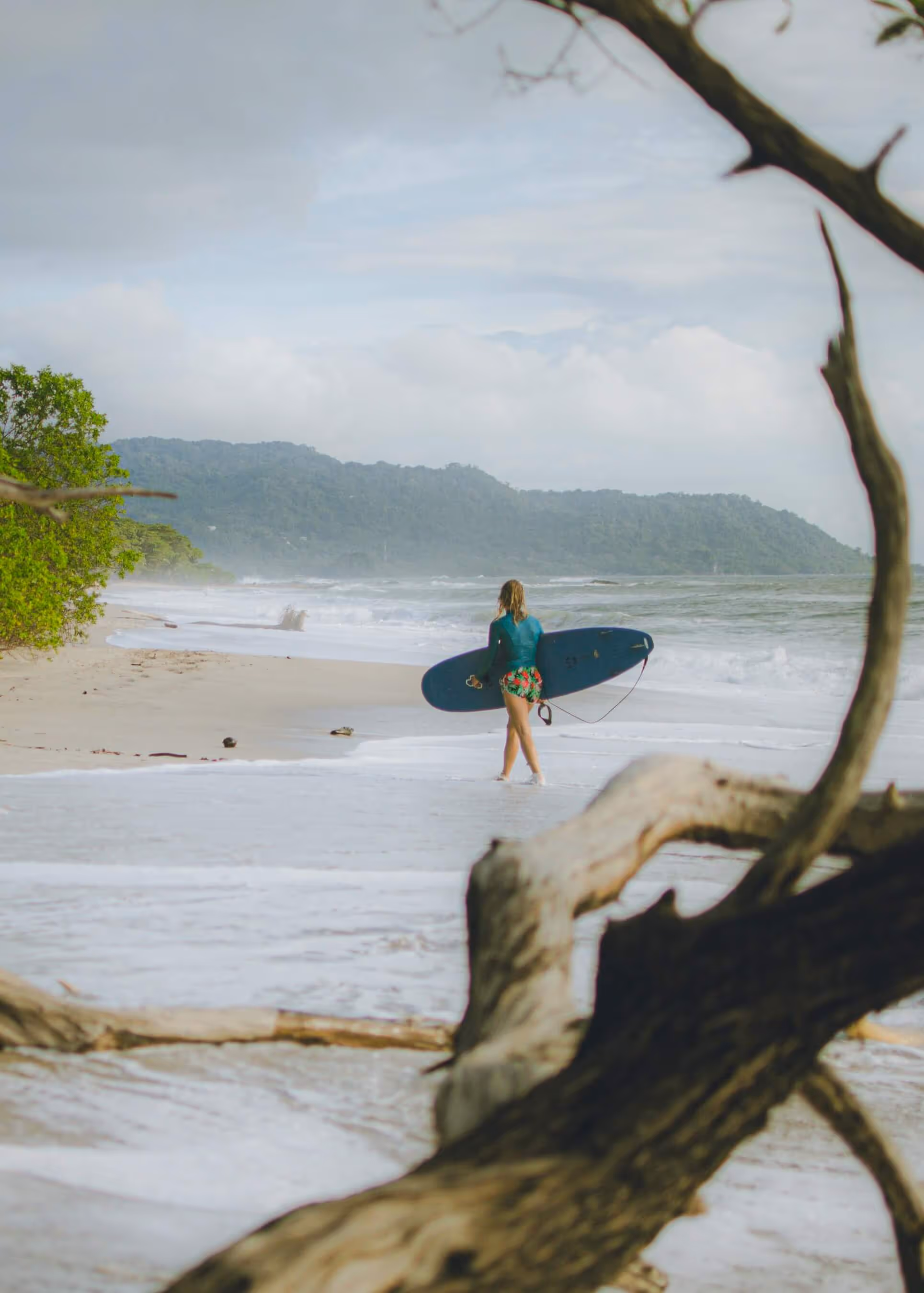 A women walking down the beach with her surfboard.