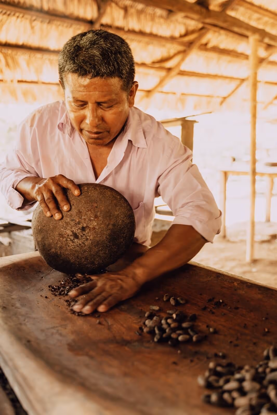 A man grinding cacao beans to with a hand made tool.