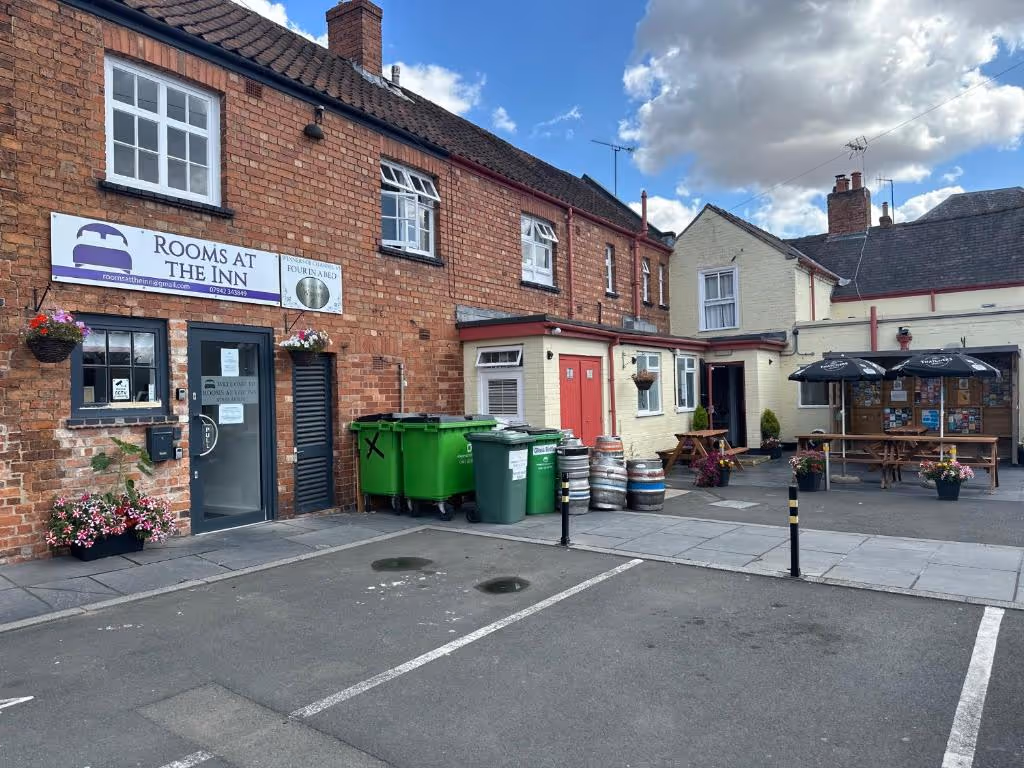 The exterior of Rooms At The Inn in Retford, UK. The red brick building features a sign for the inn and another celebrating being a "Four in a Bed" winner, with an adjacent pub patio and car park in front.